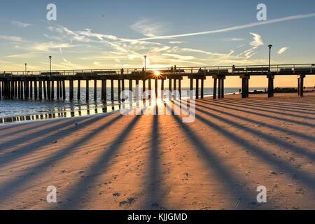 Coney Island Strand bei Sonnenuntergang mit einer lebendigen, dramatischer Himmel und lange Schatten. Stockfoto