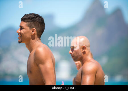 RIO DE JANEIRO - Februar 9, 2017: Brasilianischen Surfer stehen am Strand von Arpoador, der beliebten Surf spot, gegen einen Blick auf die Skyline von zwei Brüdern Mou Stockfoto