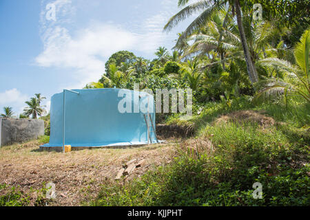 Betonplatte Wasserbehälter mit üppigem, tropischem Grün unter einem blauen Himmel mit Wolken auf dravuni Island, Fidschi Stockfoto