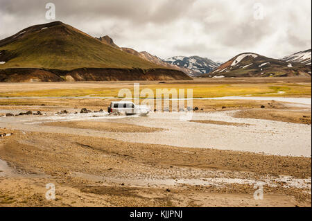 Fahrzeug 4x4, SUV Kreuzung einen Stream mit Landmannalaugar die bunten Berge noch schneebedeckt, Anfang des Sommers, Island Hochland, Europa. Stockfoto