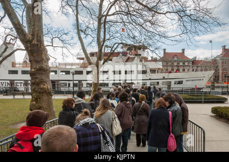 Menschen, die Schlange stehen, um an Bord der Ellis Island Fähre vom Ellis Island National Park, New York City, New York, NY, USA, abzufahren. Stockfoto