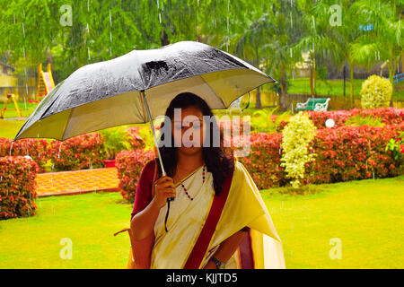 Indisches Mädchen im Sari, das im Regen mit Regenschirm läuft, Pune, Maharashtra. Stockfoto