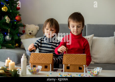 Adorable Vorschule Kinder, junge Brüder, dekorieren Lebkuchenhäuser für Weihnachten zu Hause, Weihnachtsbaum hinter Ihnen, Advent Kerzen auf den Tabl Stockfoto