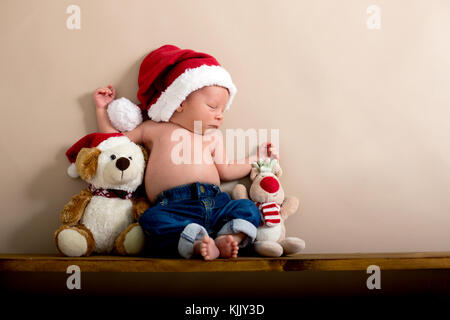 Neugeborenes Baby Boy das Tragen einer Mütze und Jeans, schlafen auf einem Regal neben Teddybären. Im Studio auf einem cremigen Hintergrund Geschossen, geschossen von abov Stockfoto