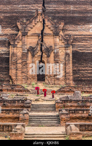 Drei buddhistischen Anfänger wandern und Halten der roten Regenschirm in mingun pahtodawgyi, Bagan, Mandalay, Myanmar Stockfoto