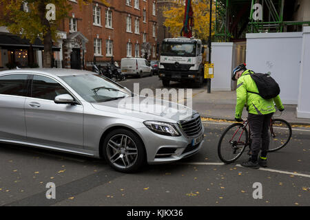 Ein verärgerter Radfahrer hält ein Kraftfahrer und sehr langsam sein Fahrrad über für Schäden nach einem Fahrer Mercedes stupste seine Hinterrad in der Frustration von starker Verkehr, am 22. November 2017 in London England prüfen zu konfrontieren. Stockfoto