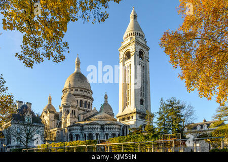 Drei Viertel der Blick auf die Basilika des Heiligen Herzen von Paris bei Sonnenaufgang im Herbst mit dem quadratischen Turm und orange Blätter im Vordergrund. Stockfoto