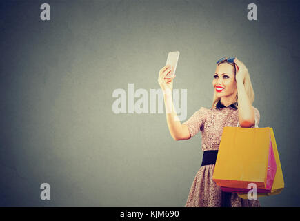 Schöne Frau shopping online unter selfies auf Handy. Mode Mädchen mit bunten Taschen auf Handy. Stockfoto