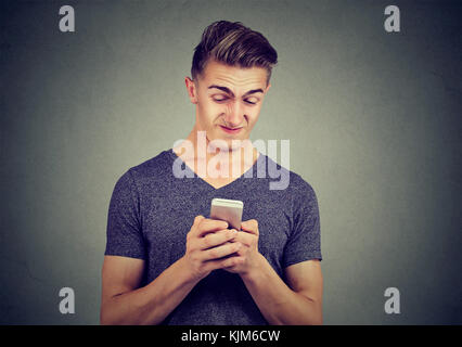 Verärgert Mann mit Handy mit Botschaft, die er isoliert auf grauen Hintergrund erhalten angewidert. Stockfoto