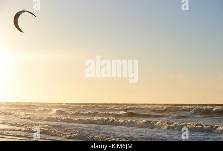 Kitesurfen in einem wilden Meer mit Wellen am Ende des Tages mit einem wunderschönen Sonnenuntergang an der Küste von Den Haag, Niederlande Stockfoto