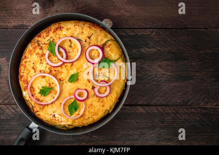 Ein Foto von einem spanischen Tortilla mit Kartoffeln und Zucchini in einem Tortillera, auf einem dunklen Holzmöbeln im Landhausstil Hintergrund mit einem Platz für Text Stockfoto