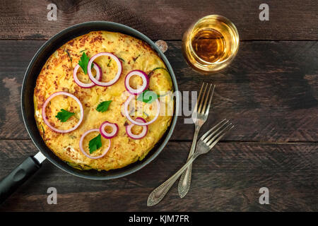 Ein Foto von einem spanischen Tortilla mit Kartoffeln und Zucchini in einem Tortillera, mit einem Glas Weißwein, zwei Gabeln und ein Platz für Text Stockfoto