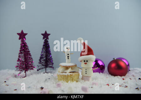 Weihnachten essen Fotografie Bild mit Marshmallows geformt als Schneemann mit Iced auf Lächeln und Schnee mit Schwamm Creme fee Kuchen und Baum Flitter Stockfoto