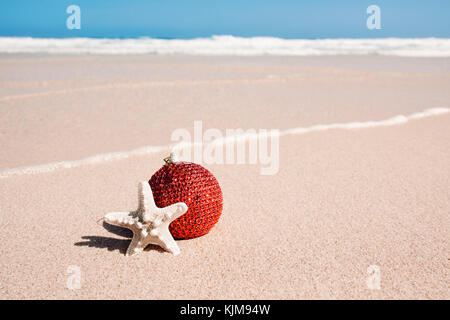 Eine elegante Red christmas Ball und ein Seestern in den Sand des Strandes, neben der Küste Stockfoto