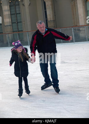 Ein Kind und ein Erwachsener halten Hände beim Schlittschuhlaufen auf der Eisbahn in Brighton Stockfoto