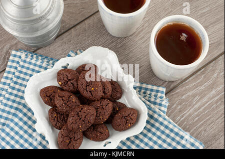 Rustikale Kekse mit Schokolade und Nüsse in Keramik Schüssel mit zwei Tassen Tee, Zucker und Stoffservietten Stockfoto