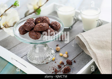 Rustikale cookies mit Kakao und Pistazien auf Kuchen - stehen für Süßigkeiten mit Holz- Fach zwei Tassen Milch, Tuch, Serviette und weißen Blüten im Hintergrund Stockfoto