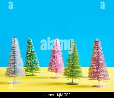 Miniatur bunte Weihnachtsbäume auf blauem und gelbem Hintergrund, Platz für Text. Stockfoto