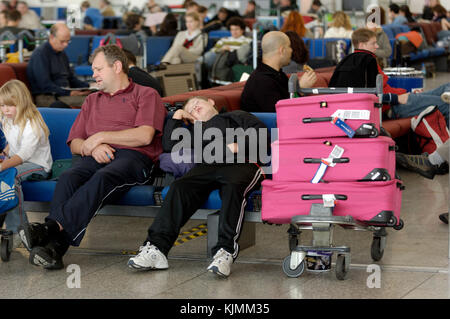 Ein Passagier schlafen auf einer Sitzbank im Hauptterminal neben einem vollen Wagen Last von rosa Koffer Gepäck Stockfoto