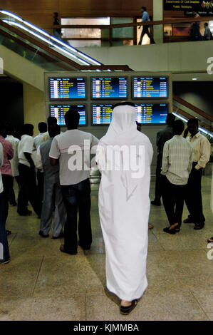 Männer greeters und Freunde im Terminal 1 Ankunft warten Bahnhofshalle auf Flug info-Bildschirme, einige in arabischer Kleidung Stockfoto