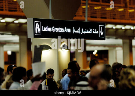 Greeters und Geschäftsleute warten unter einem "Ladies Greeters" mehrsprachige Schild in der Ankunftshalle des Terminal 1. Stockfoto