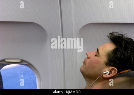 Mann schlafen mit Ohrhörer in seiner Wirtschaft - Klasse Sitzplatz BRS-GVA Stockfoto