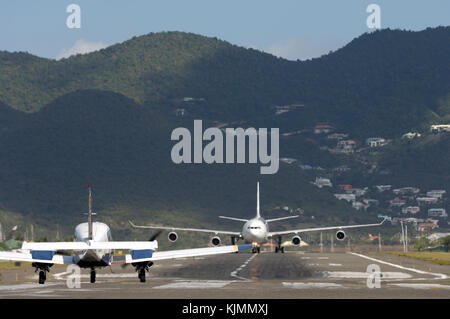 Ein Airbus A340 Rollen backtracking die Start- und Landebahn mit einer Piper Aztec jet warten zu nehmen - Vom gleichen Start- und Landebahn in Sint Maarten. Stockfoto