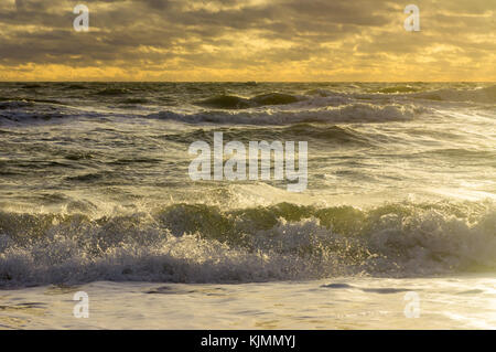 Kleine Wellen in der unruhigen Meer rollen am Ufer mit Schaumstoff unter dem bewölkten Himmel Stockfoto