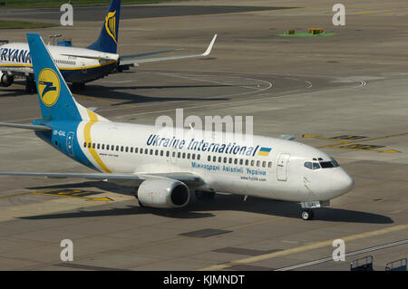 Eine Ukraine International Airlines Boeing 737-300 Rollen auf dem Vorfeld mit Ryanair 737-800 hinter Stockfoto