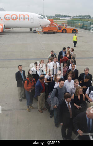 Geschäftsleute und andere Männer und Frauen Passagiere warten in einer Warteschlange auf dem Vorfeld, an Bord der 737 über die airstairs für den Flug EZY 2552 mit Reisetasche Stockfoto