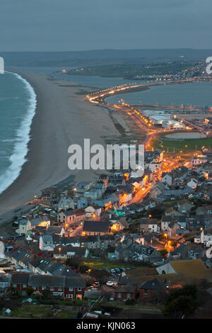 Underhill (chiswell) an der Portland in der Morgendämmerung, Auto Scheinwerfer Trails und Straßenbeleuchtung entlang Chesil Beach in Richtung weymouth Hafen zeigen führende Stockfoto