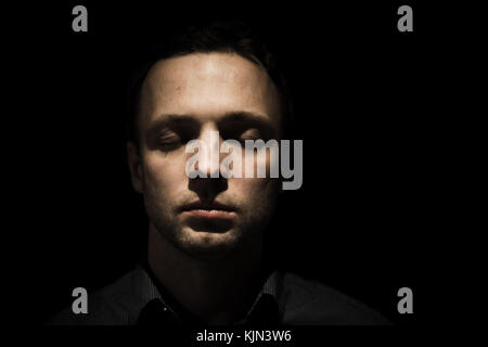 Closeup studio Gesicht Porträt der jungen Erwachsenen europäischen Mann mit geschlossenen Augen über schwarzen Hintergrund isoliert, Low Key Foto Stockfoto