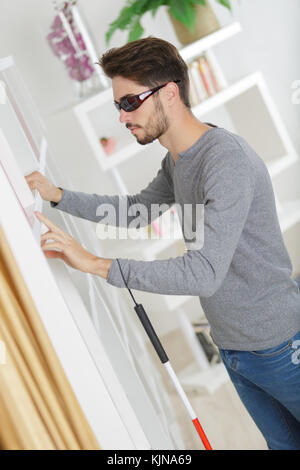 Blinder Mann mit weißem Stick und dunklen Brillen zu Hause Stockfoto