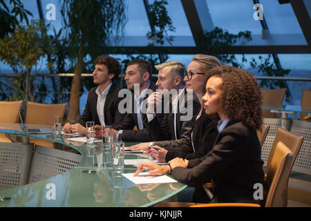 Eine Gruppe von Geschäftsleuten sitzen an einem Tisch in einer Linie und Diskutieren. Stockfoto