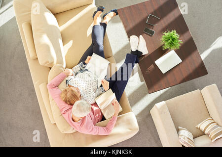 Hohe Betrachtungswinkel von einer entspannten senior Paar lesen zusammen ein Buch auf dem Sofa zu Hause. Stockfoto
