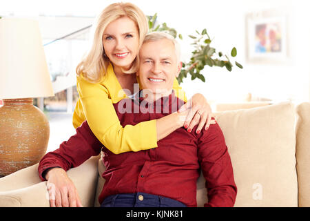 Schuss eine liebevolle Frau ihrem Mann umarmt von hinten während zu Hause im Wohnzimmer. Stockfoto
