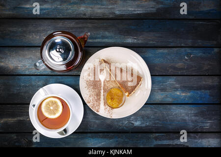 Stück Käsekuchen mit Marmelade und Tee Wasserkocher mit Zitrone auf einem farbigen Hintergrund Holz. top View Stockfoto