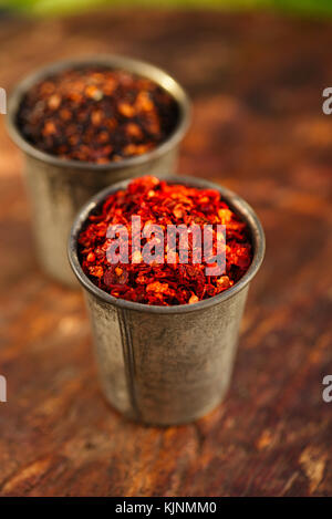 Red Hot Chili und chipotle jalapeno Geräuchertes chili Flocken in Vintage schimmel Zinn auf strukturierte woden Hintergrund Stockfoto