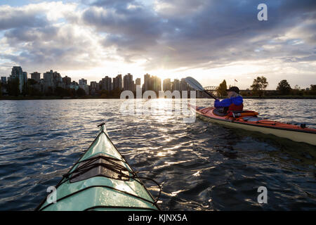 Abenteuerliche Mädchen ist Kajak bei einem Sonnenaufgang mit Sicht auf die City Skyline im Hintergrund. in Vancouver, British Columbia, Kanada. Stockfoto