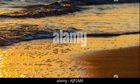 Bunte Formen durch brechende Wellen auf einem Sandstrand und Sonne Reflexionen bei Sonnenuntergang erstellt Stockfoto