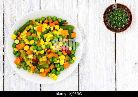 Weiße Platte mit gemischter Salat. Weiß Holz- Hintergrund. Der Kaktus auf dem Tisch. Ansicht von oben. Stockfoto