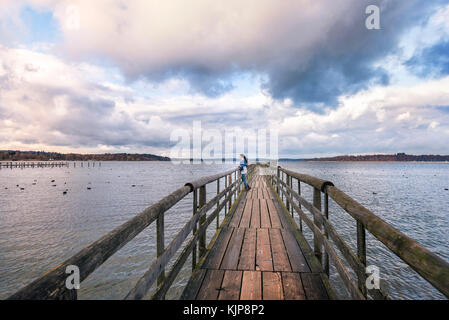 Junge Frau, die auf eine alte Holzbrücke, meditieren und bewundern Sie die Aussicht auf den Chiemsee, am Nachmittag, in der Nähe von Rosenheim, Deutschland Stockfoto