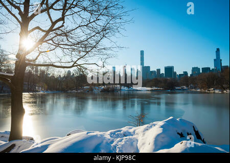 Blick auf die Skyline von Manhattan in das Eis des zugefrorenen Central Park See spiegelt die Morgen nach einem Winter Schnee Sturm in new york city Stockfoto