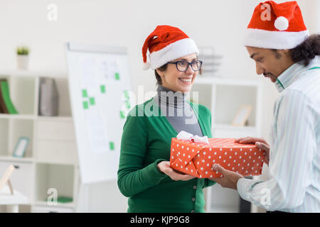 Geschäftsfrau schenkt Weihnachtsgeschenk in großer roter Geschenkbox an einen verwunderten Kollegen Stockfoto