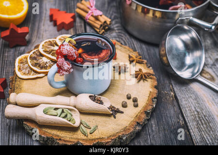 Glühwein in einem eisen Becher und Zutaten auf einem hölzernen Hintergrund Stockfoto