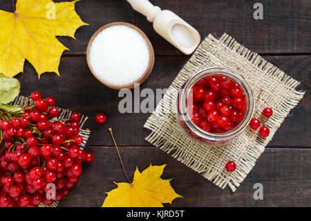 Rot saftige Beeren eines Viburnum mit Zucker in einem Glas auf einem dunklen Hintergrund. für die Herstellung von Marmelade, Tee. Heilpflanze. Stockfoto