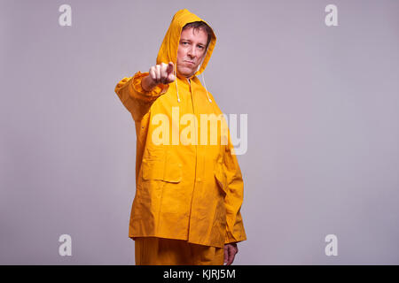 Eine ernste Mann mittleren Alters stehend in einem gelben Regenmantel und zeigte in der Kamera Stockfoto
