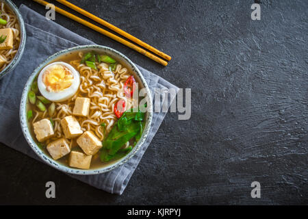 Japanische Ramen Suppe mit Tofu und Ei auf dunklem Stein Hintergrund. Miso Suppe mit Ramen Nudeln und Tofu in Keramik Schüssel, asiatische Speisen. Stockfoto