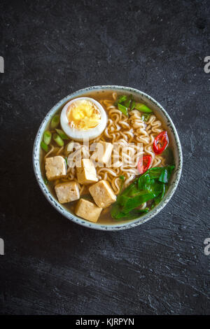 Japanische Ramen Suppe mit Tofu und Ei auf dunklem Stein Hintergrund. Miso Suppe mit Ramen Nudeln und Tofu in Keramik Schüssel, asiatische Speisen. Stockfoto
