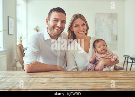 Stolz darauf, junge Mutter und Vater an einem Tisch zusammen zu Hause sitzen schaukelnd ihre neugeborene Tochter Stockfoto